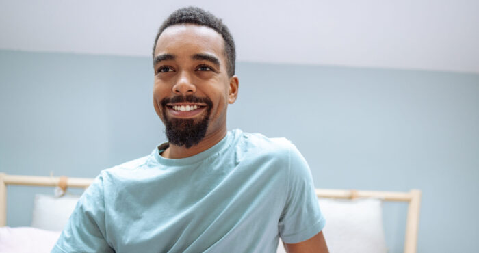 Handsome young African American man waking up in bed with smile