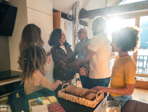 Mixed race grandparents enjoy a visit with their Caucasian and Black daughter, her husband and their mixed race children in a sunny, modern kitchen.