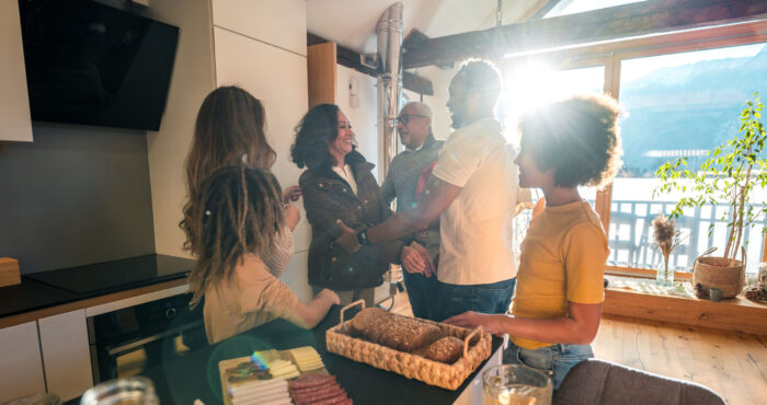 Mixed race grandparents enjoy a visit with their Caucasian and Black daughter, her husband and their mixed race children in a sunny, modern kitchen.