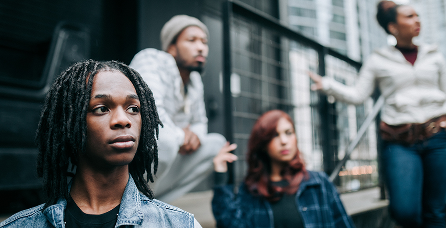 Group of four diverse young people standing by a metal fence, looking into the distance with serious expressions on their faces.